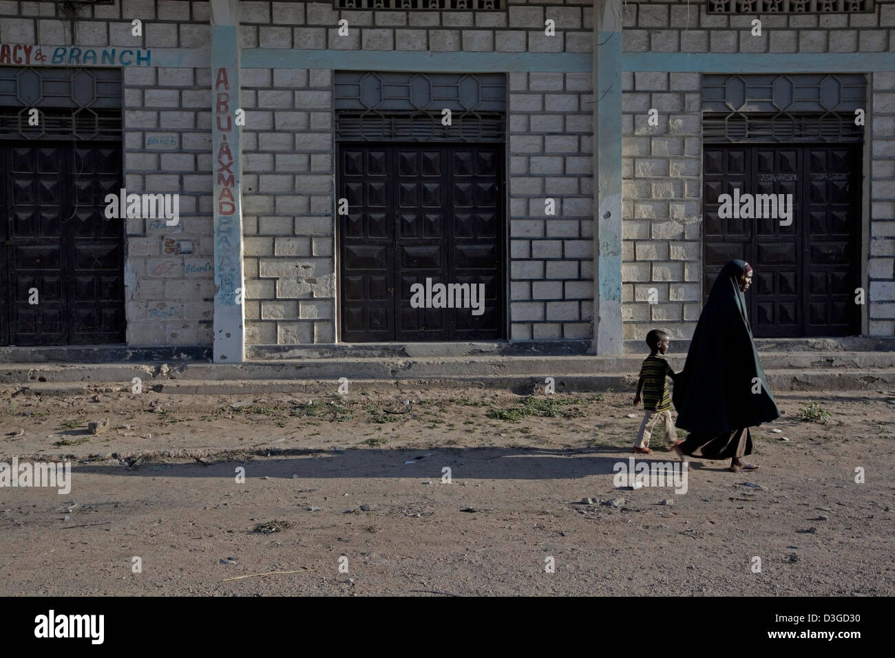 Eine somalische Frau trägt ein Kopftuch und ihr Sohn gehen vorbei an einer geschlossenen Apotheke. Stockfoto