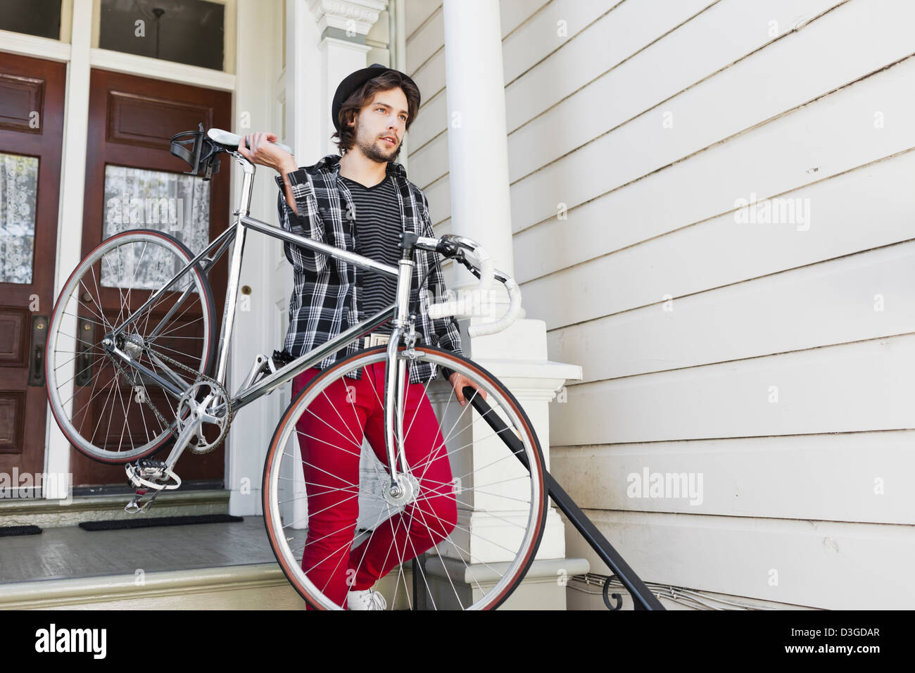 Hipster und Beatniks - ein Junge Hipster-Mann in engen Jeans, kariertes Hemd und Hut zu Hause in seinem fixed Gear Bike verlassen. Stockfoto