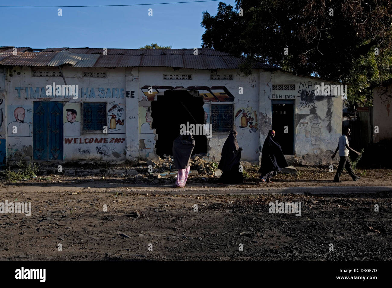 Drei Somalische Frauen in ein Kopftuch und ein Mann gekleidet gehen vorbei an einem stillgelegten kriegszerstörten Gebäude im Zentrum von Mogadischu. Stockfoto
