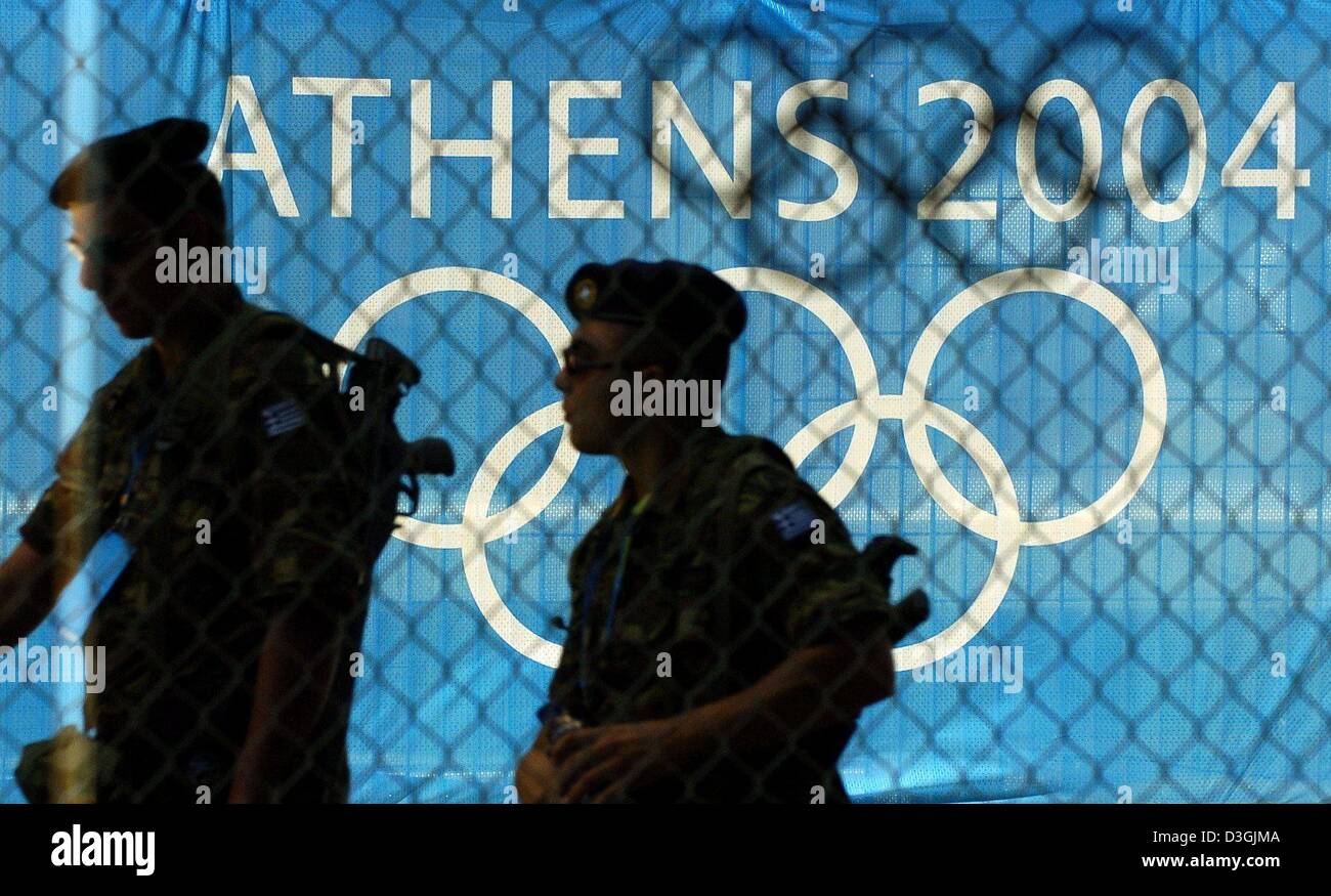 (Dpa) - bewaffnete Soldaten patrouillieren vor Olympia-Logo auf einem Zaun, der das Olympiagelände in Athen, Griechenland, 2. August 2004 umgibt. Im Vorfeld der Olympischen Spiele, die von 13 August bis 29. August 2004 stattfinden wird, werden alle Olympische Sportstätten rund um die Uhr bewacht. Insgesamt 70.000 Sicherheitskräfte werden einerseits für die Sommerspiele um Terroranschläge zu verhindern. Securit Stockfoto