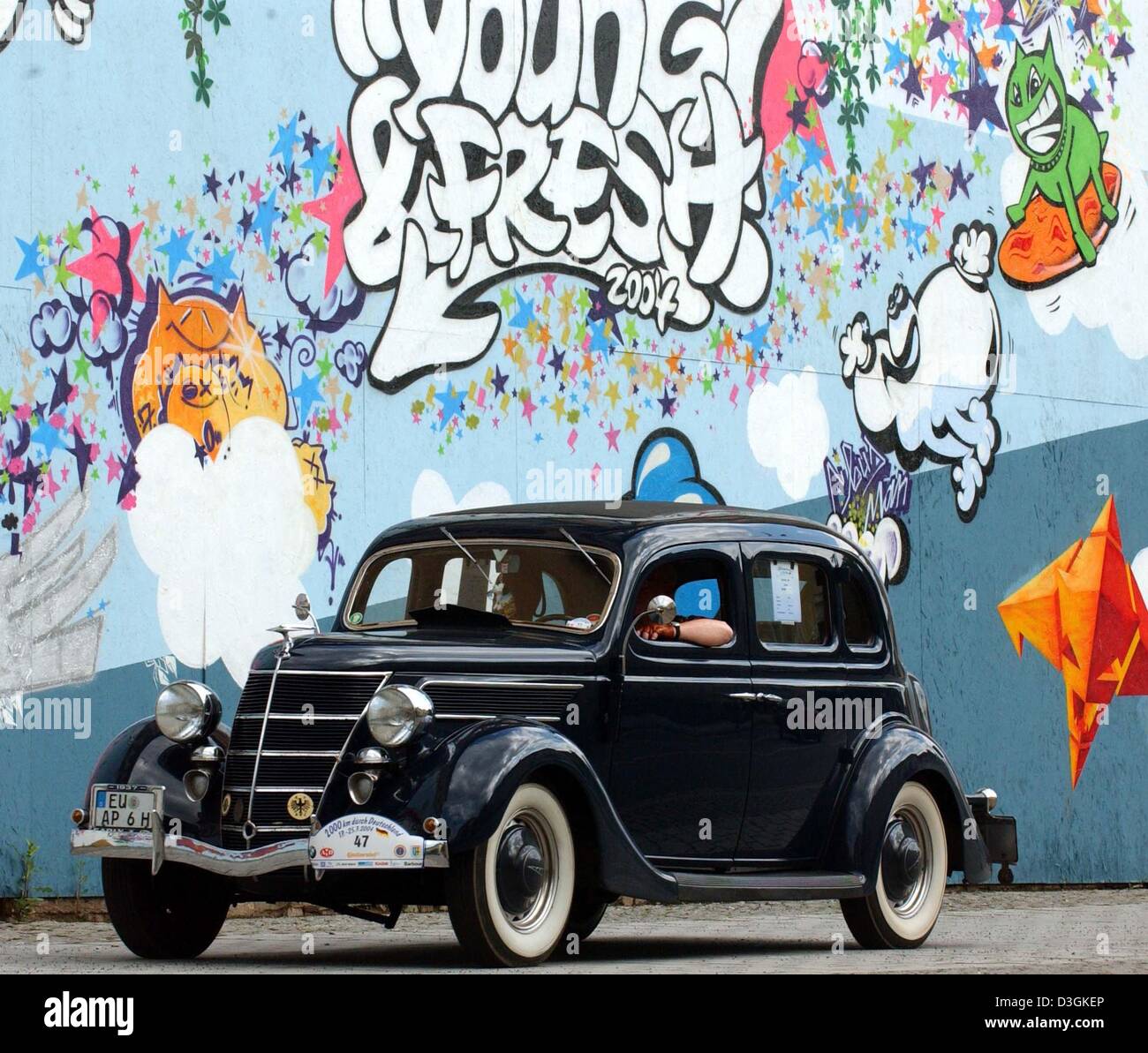 (Dpa) - A Ford V8-48 Oldtimer ab 1937 fährt vorbei an Graffiti besprühten Wand während des Oldtimer-Tou-Festivals in Meiningen, Deutschland, 19. Juli 2004. Stockfoto