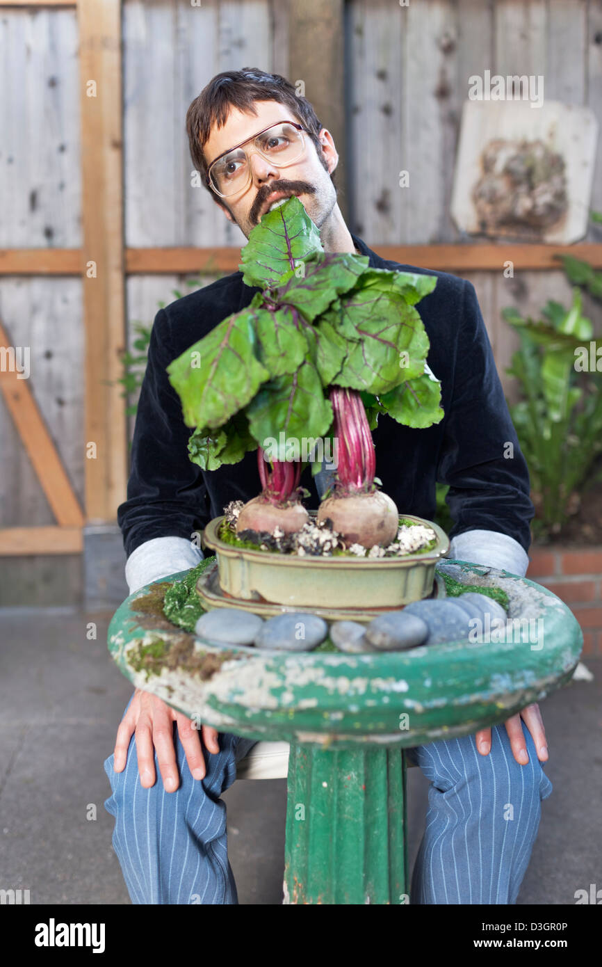 Hipster und Beatniks - ein Junge Hipster-Mann mit Schnurrbart und Brille noch essen Rüben auf gepflanzt ein Vogelbad in seinem eigenen Garten Stockfoto