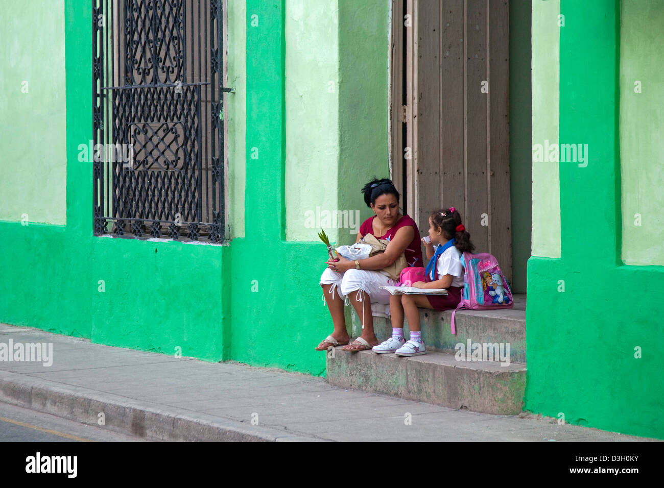 Mutter und Tochter in Schuluniform sitzen vor Haustür Pastell farbigen Haus in Camagüey, Kuba, Karibik Stockfoto