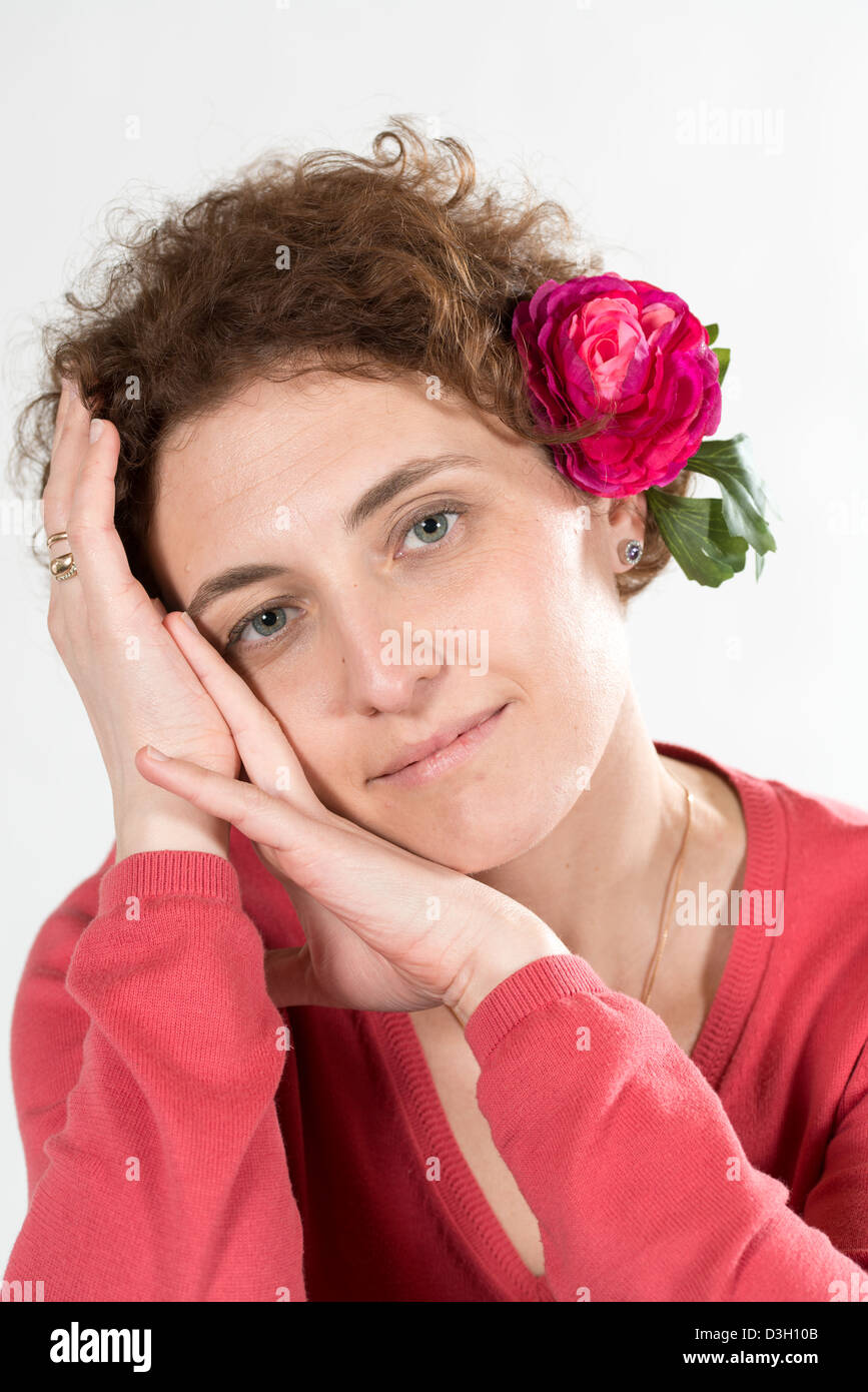 junge lockig Frau trägt Rosa Kleidung und rote Blume im Haar Stockfoto