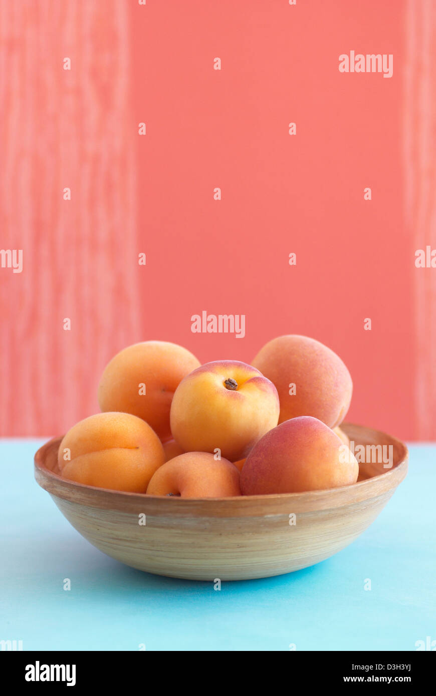 Aprikosen in Holz Schüssel mit orangefarbenem Hintergrund, Petrol / Tischset Stockfoto