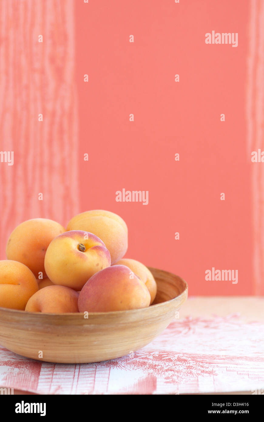 Aprikosen im Holz Schale mit orangefarbenen und weißen Stoff Tischset und Orange Hintergrund Stockfoto