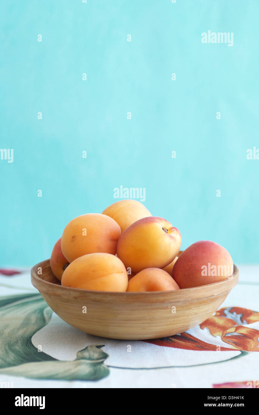 Aprikosen im Holz Schale mit bemalten Tulpe Stoff und blau Hintergrund Stockfoto
