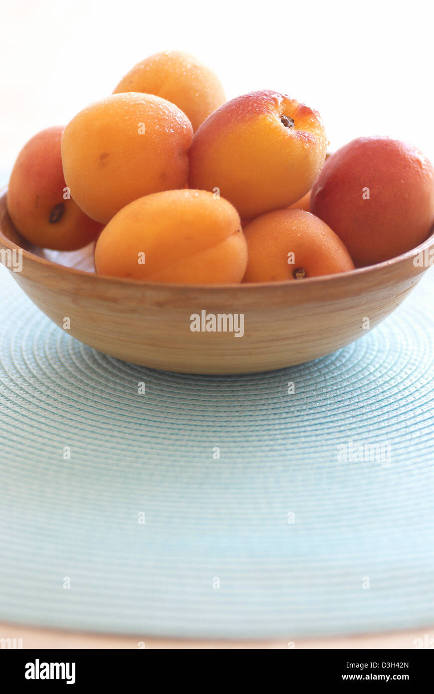 Aprikosen im Holz Schüssel auf hellblau Kreis Tischset Stockfoto