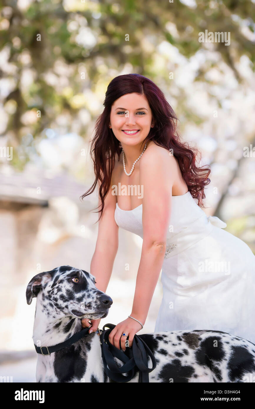 Lächelnde Braut im Hochzeitskleid mit schwarzen und weißen Dogge Hund Stockfoto