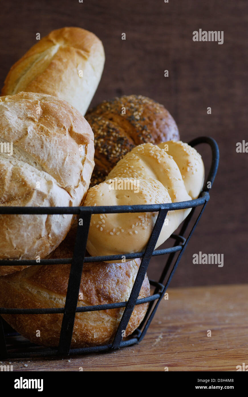 Artisan Brot Brote in Metall Drahtkorb auf Holz Schneidebrett, Sauerteig, Französisch, Mohn, Sesam, Mini-Sauerteig-Brot Stockfoto