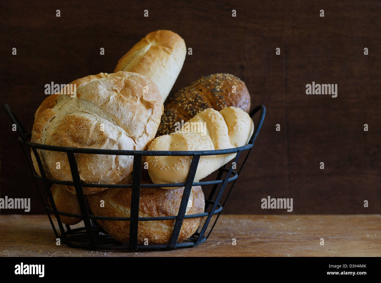 Artisan Brot Brote in Metall Drahtkorb auf Holz Schneidebrett, Sauerteig, Französisch, Mohn, Sesam, Mini-Sauerteig-Brot Stockfoto