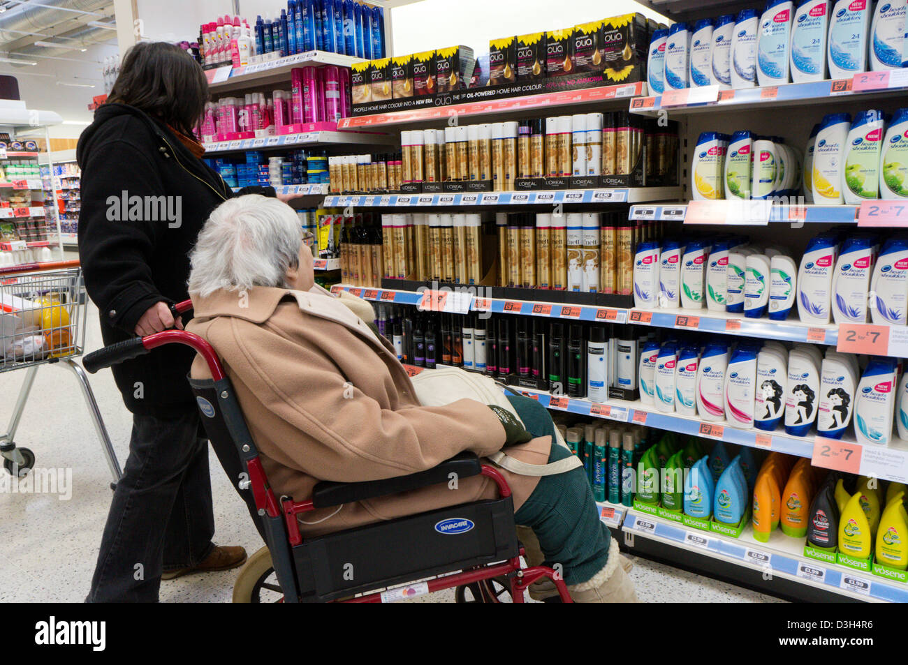 Eine ältere Dame im Rollstuhl und ihre Betreuer oder Helfer Blick auf Produkte Haare und Shampoo in einem Supermarkt. Stockfoto