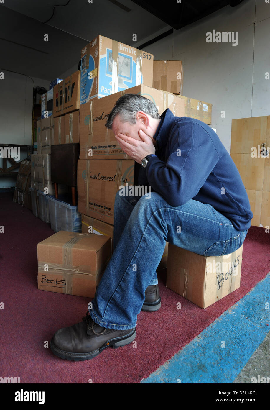 MANN MIT KOPF IN HÄNDEN MIT HAUFEN VON UMZUGSKARTONS RE HAUS BEWEGEN BEWEGEN RÜCKNAHME OBDACHLOSEN HEIM RÄUMUNG RELOCATION STRESS UK Stockfoto