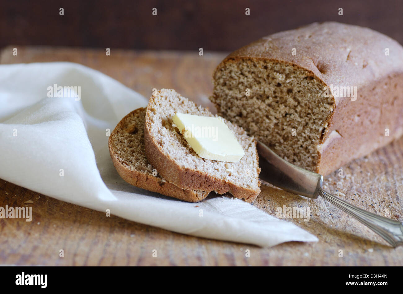 Artisan Brot, ganze Wheat Bread Loaf, Holzzuschnitt Board Scheibe Brot mit Butter, weiße Stoffserviette, mit Buttermesser Stockfoto