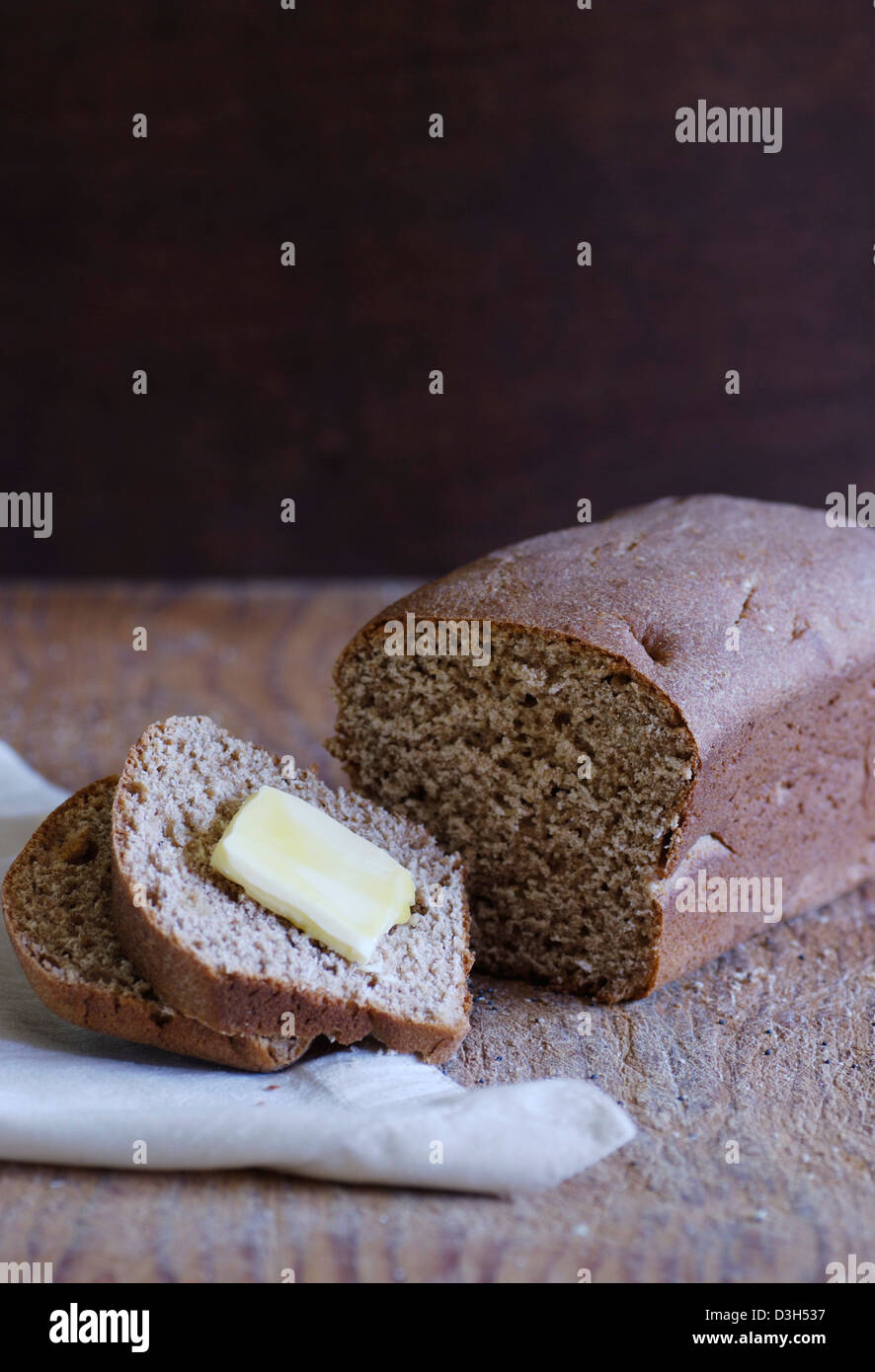 Artisan ganze Weizenbrot Brotlaib, Schneiden von Holz Brett Scheibe Brot mit Butter, weißen Stoffserviette Stockfoto