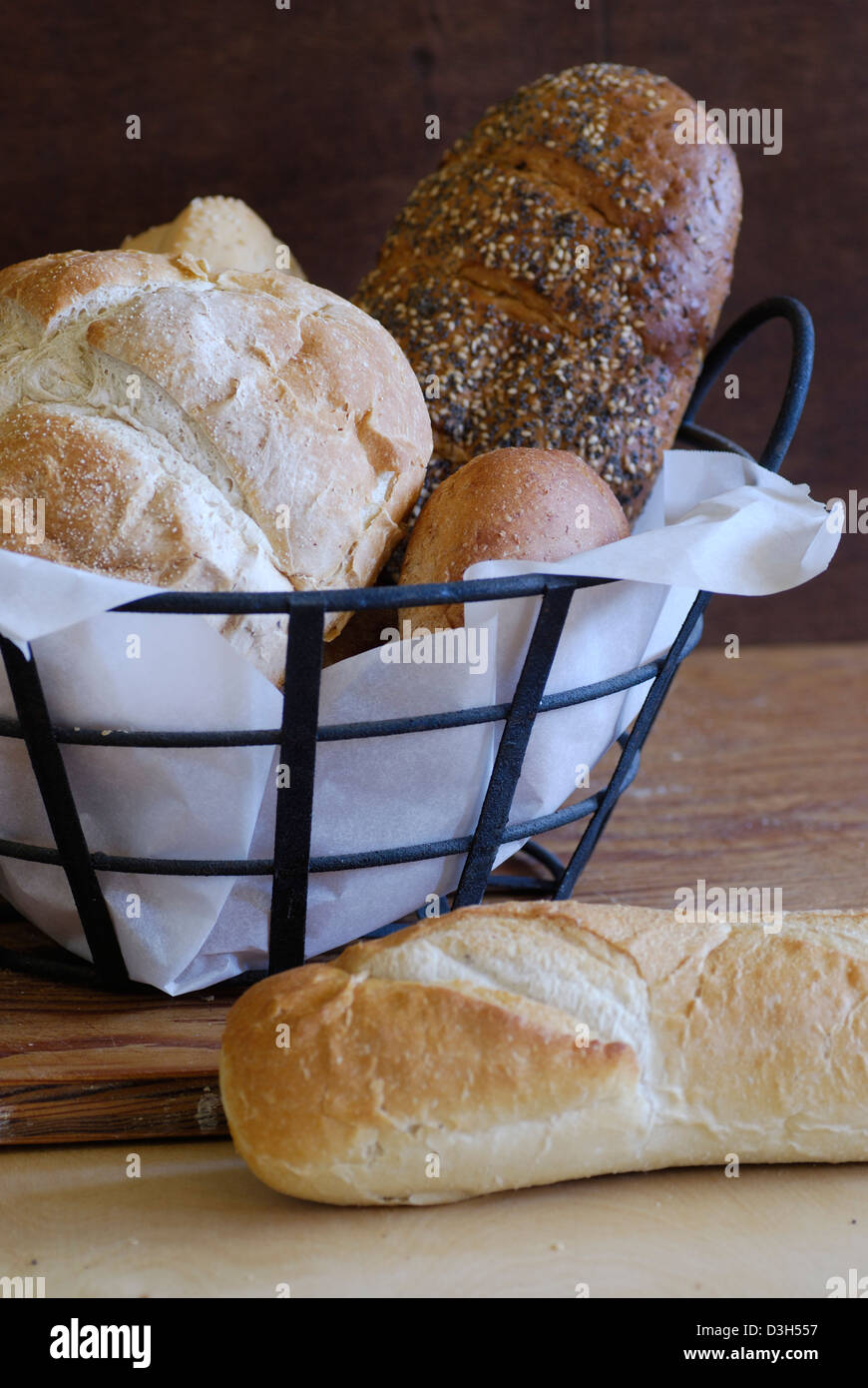 Artisan Brot Brote in Metall Korb-Einstellung auf Holz Schneidebrett Stockfoto