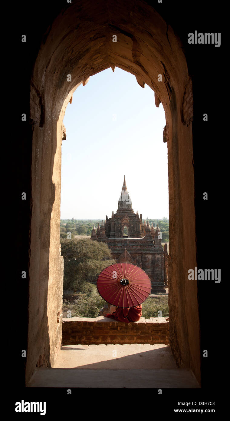 Junge Novize und Sonnenschirm, gerahmt in einem Torbogen Bagan-Tempel. Stockfoto