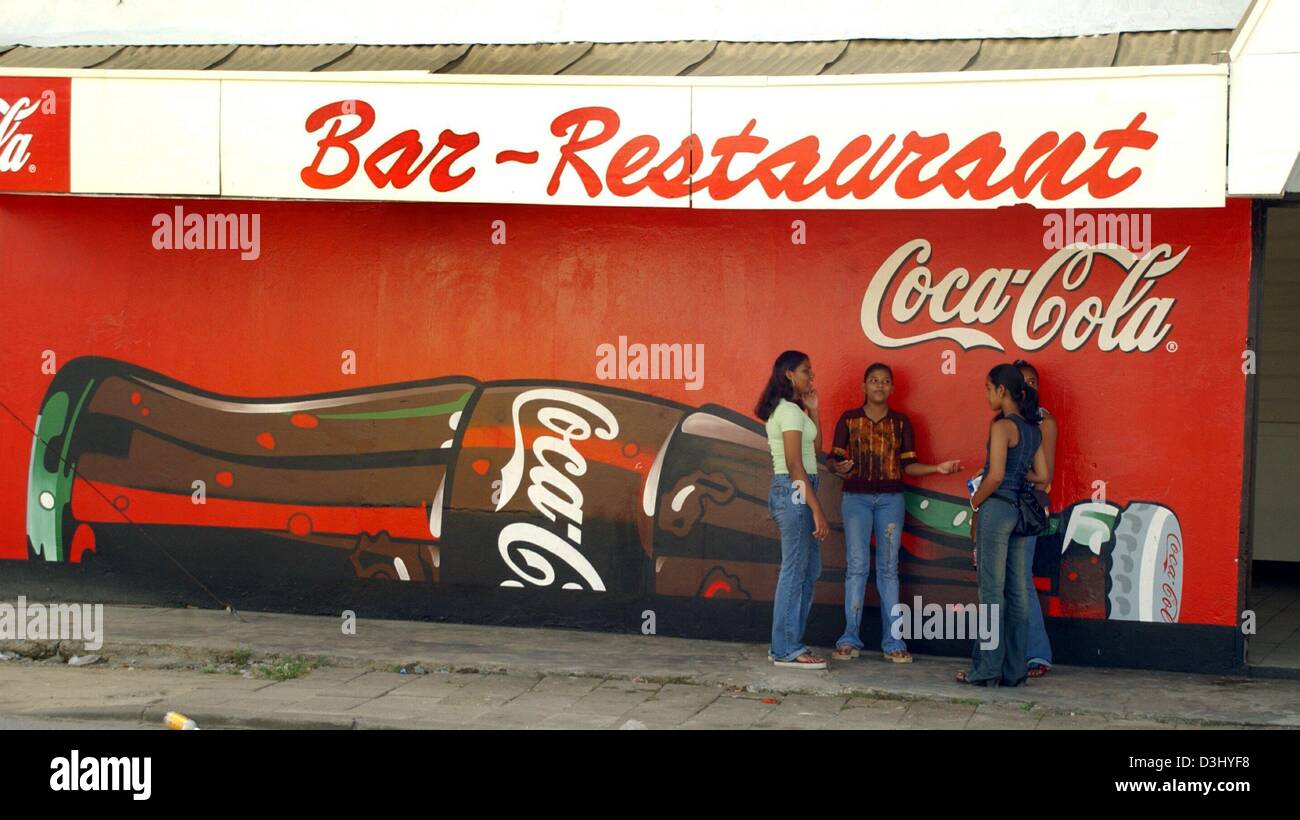 (Dpa) - eine Gruppe Jugendlicher miteinander chatten wie sie stehen vor der Außenwand eine Bar und ein Restaurant verfügt über eine riesige Coca-Cola-Werbung in Paramaribo, der Hauptstadt von Suriname, Südamerika, 26. November 2003. Stockfoto