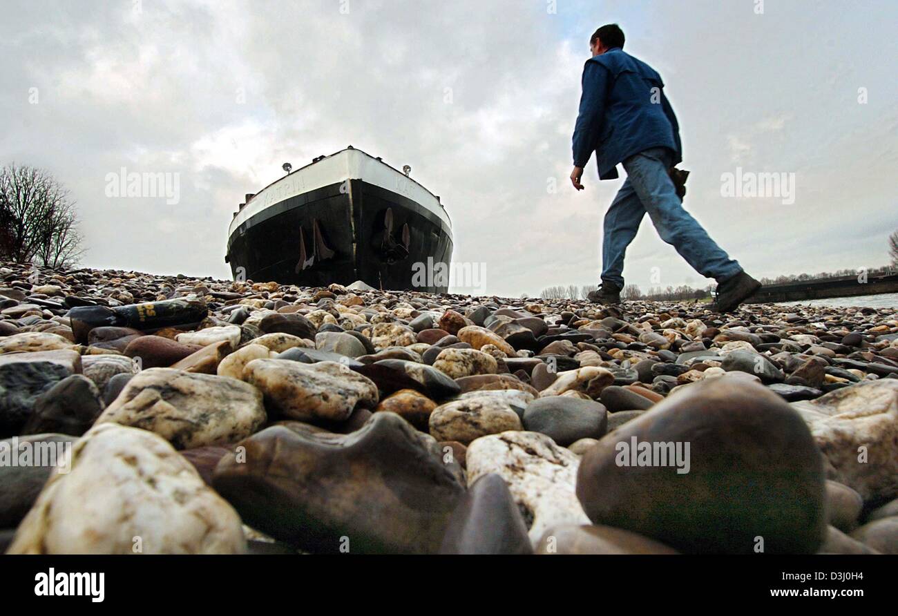 (Dpa) - ein Mann geht entlang des Flussbettes des Rheins vorbei an dem gestrandeten Tanker Flussschiff "Romulus" in Köln, Deutschland, 9. Januar 2004. Das Boot durch den niedrigen Wasserstand des Flusses gestrandet. Trotz starken Regenfällen in den letzten Tagen, die der Wasserstand noch 1,72 Meter markiert ist, jedoch erhöht leicht auf einer täglichen Basis. Stockfoto