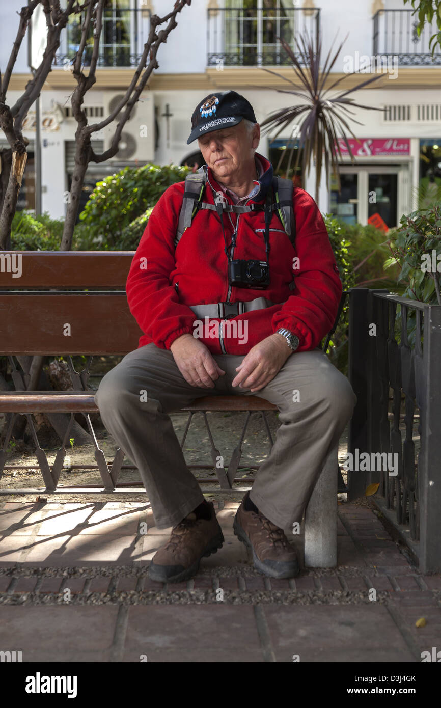 Senior mit einer Kamera männlichen ringsum seinen Ansatz und ein Rucksack verschiebt auf einer Parkbank Stockfoto
