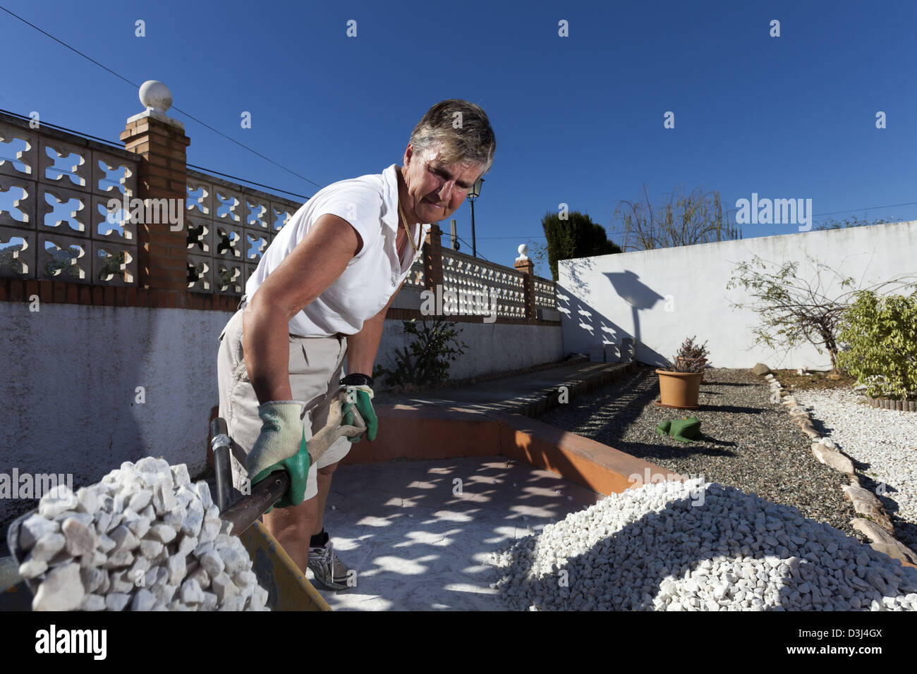 Reife Frauen Schwitzen mit den Bemühungen der Schaufeln Kies in eine Schubkarre Stockfoto