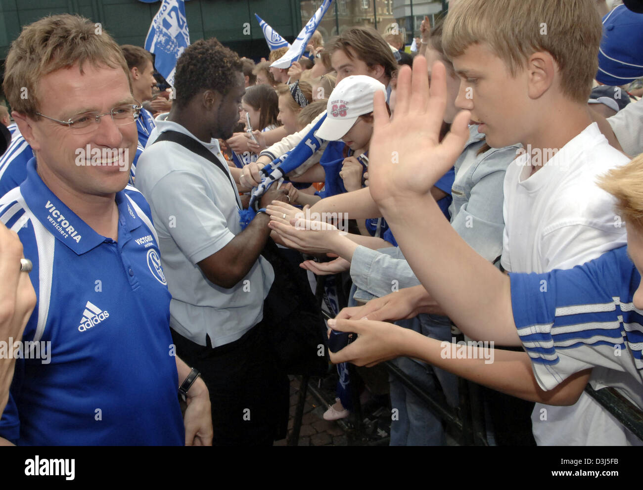 (Dpa) - FC Schalke 04 Chef-Trainer Ralf Rangnick (L) und Spieler Gerald Asamoah (C) zu Fuß durch Linien der Schalke-Fans in Gelsenkirchen, Deutschland, 29. Mai 2005. Fast 2.000 Fans jubelten die Spieler trotz der Niederlage im Deutsch-Cup-Finale gegen den FC Bayern München. Stockfoto