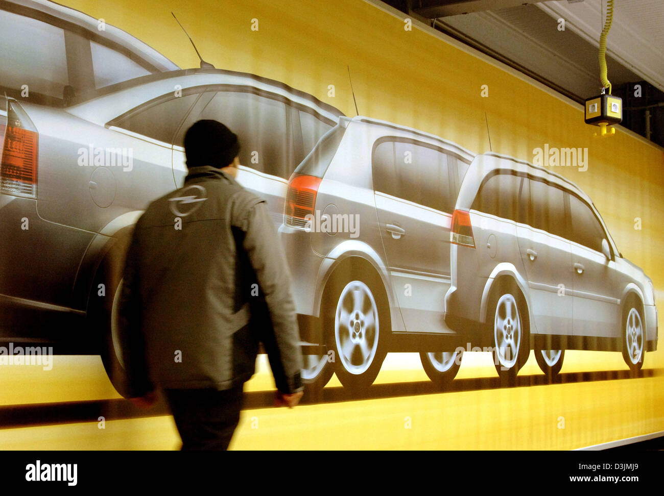 (Dpa) - Spaziergänge ein Mitarbeiters Pas, die ein großes Plakat mit von Autohersteller Opel im Werk in Rüsselsheim, Deutschland, 4. März 2005 Modellen. Nach monatelangen Verhandlungen kam der Unternehmensleitung und dem Betriebsrat zu einer Einigung. Das Produktionswerk in Bochum baut fünftürige Astra-Limousine. Stockfoto