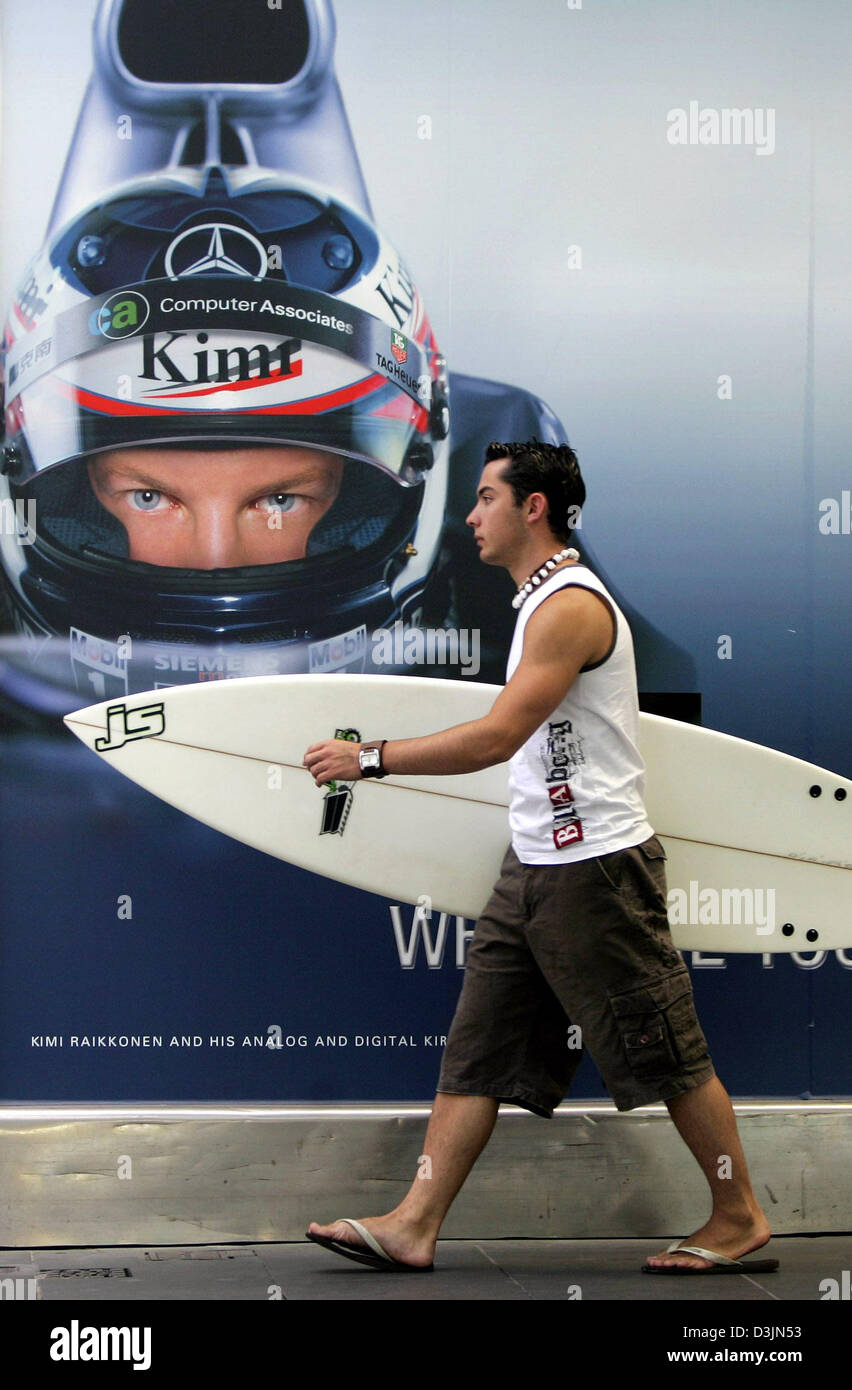 (Dpa) - verweilt Robbie ein Surfer mit seinem Surfbrett vorbei ein Werbeplakat mit dem Bild des finnischen Formel-1 pilot Kimi Raeikkoenen von McLaren-Mercedes in Melbourne, Australien, Dienstag, 1. März 2005. Das erste Rennen der 2005 Formel-1-Saison, den Australian Grand Prix startet am Sonntag. Stockfoto