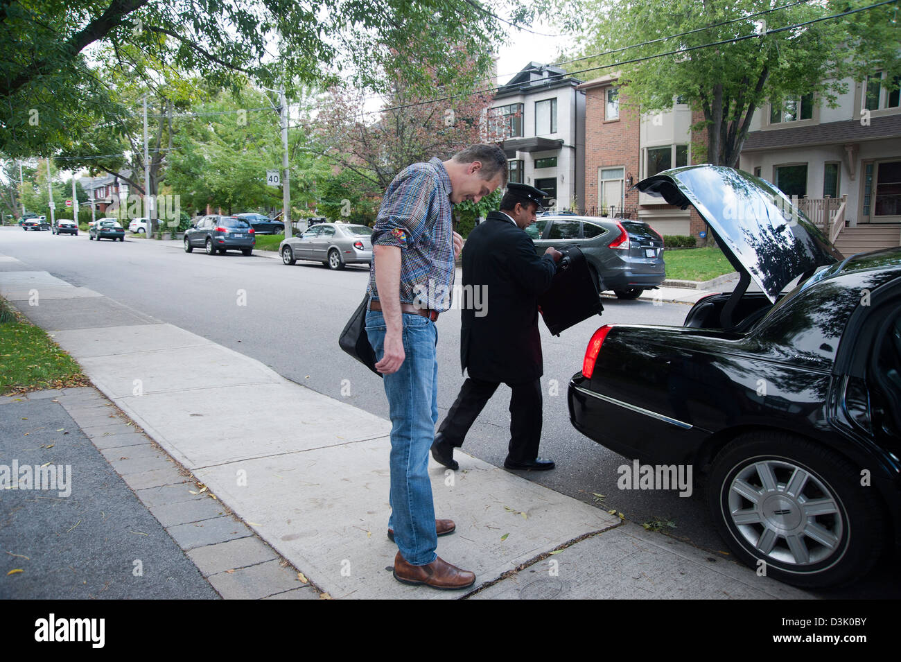 Ein Mann wartet auf Bürgersteig während uniformierten Chauffeur bringt sein Gepäck im Kofferraum des Autos Stockfoto