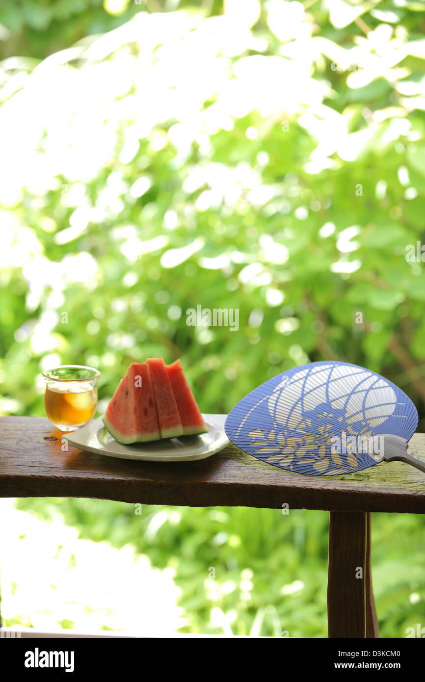 Wassermelone-Getränk und Papier-Fan auf einer Holzbank Stockfoto