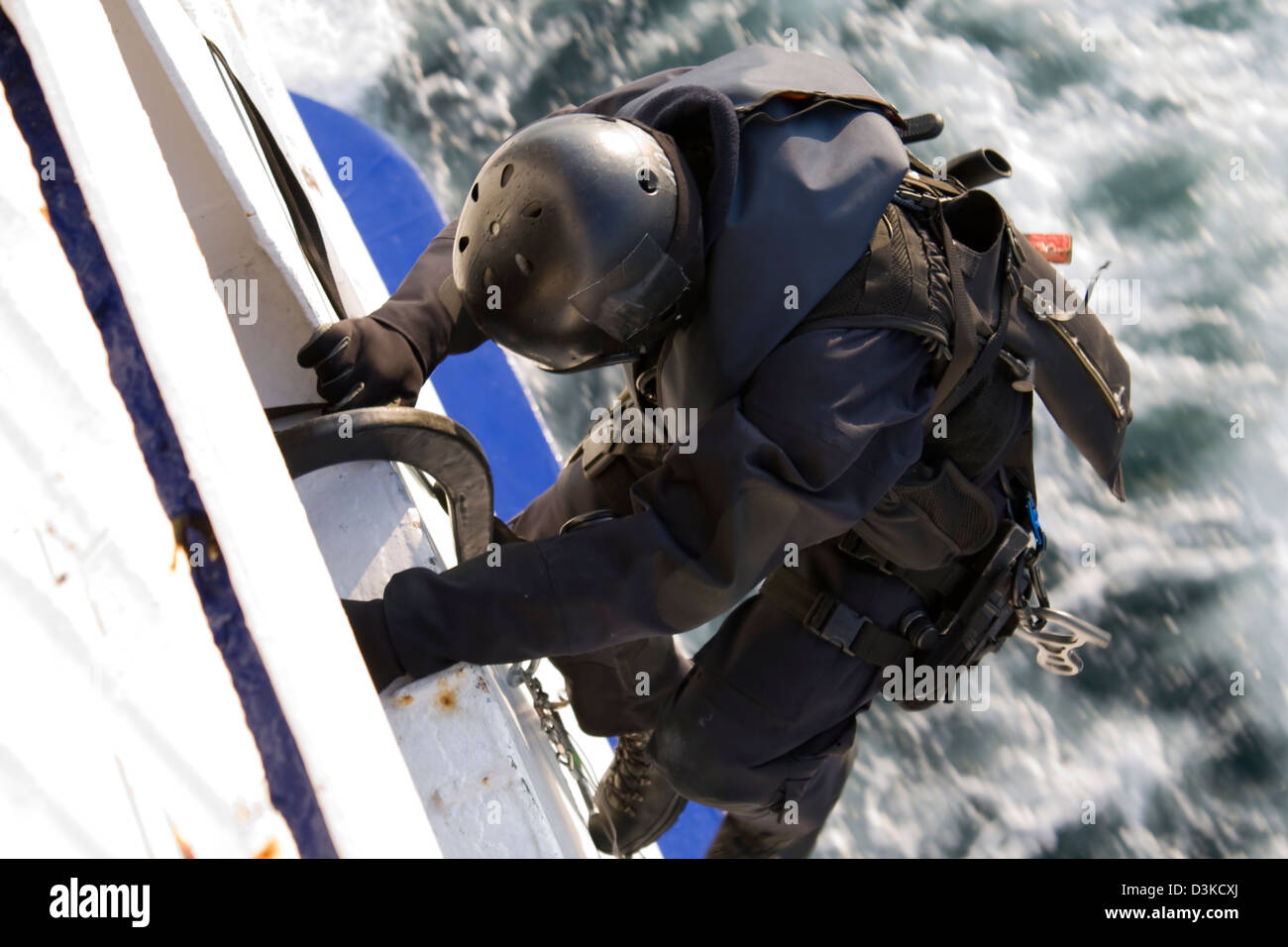 Ein Spezialeinheit (SWAT) Agent klettert die Seite von einem beweglichen Schiff über eine aufrollbare Leiter. Stockfoto