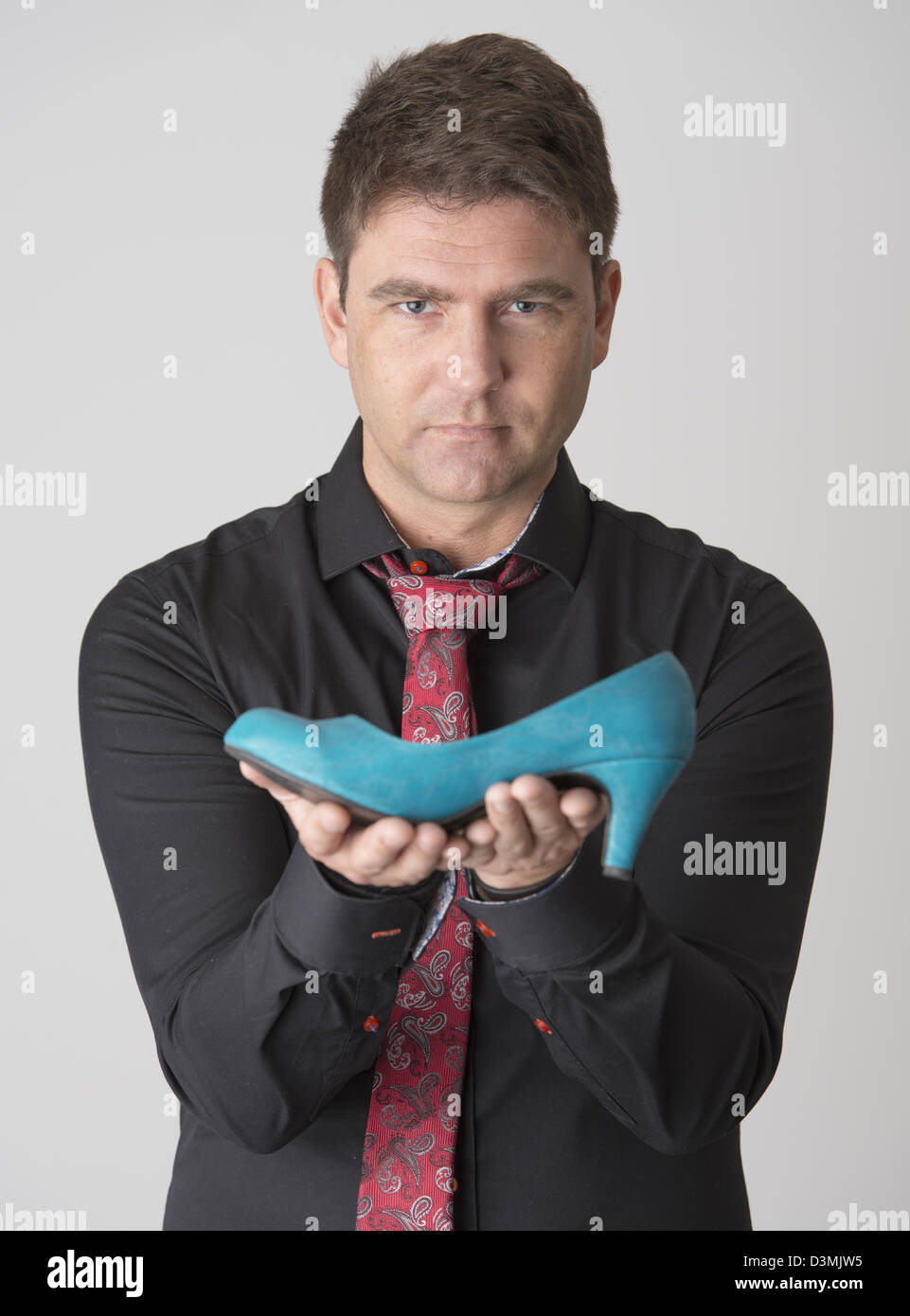 Schwere Männchen schwarzes Hemd mit roter Krawatte hält blau Womans Schuh Stockfoto