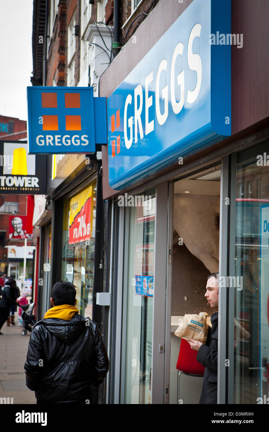 Mann isst Kuchen in Greggs Shop Tür Stockfoto