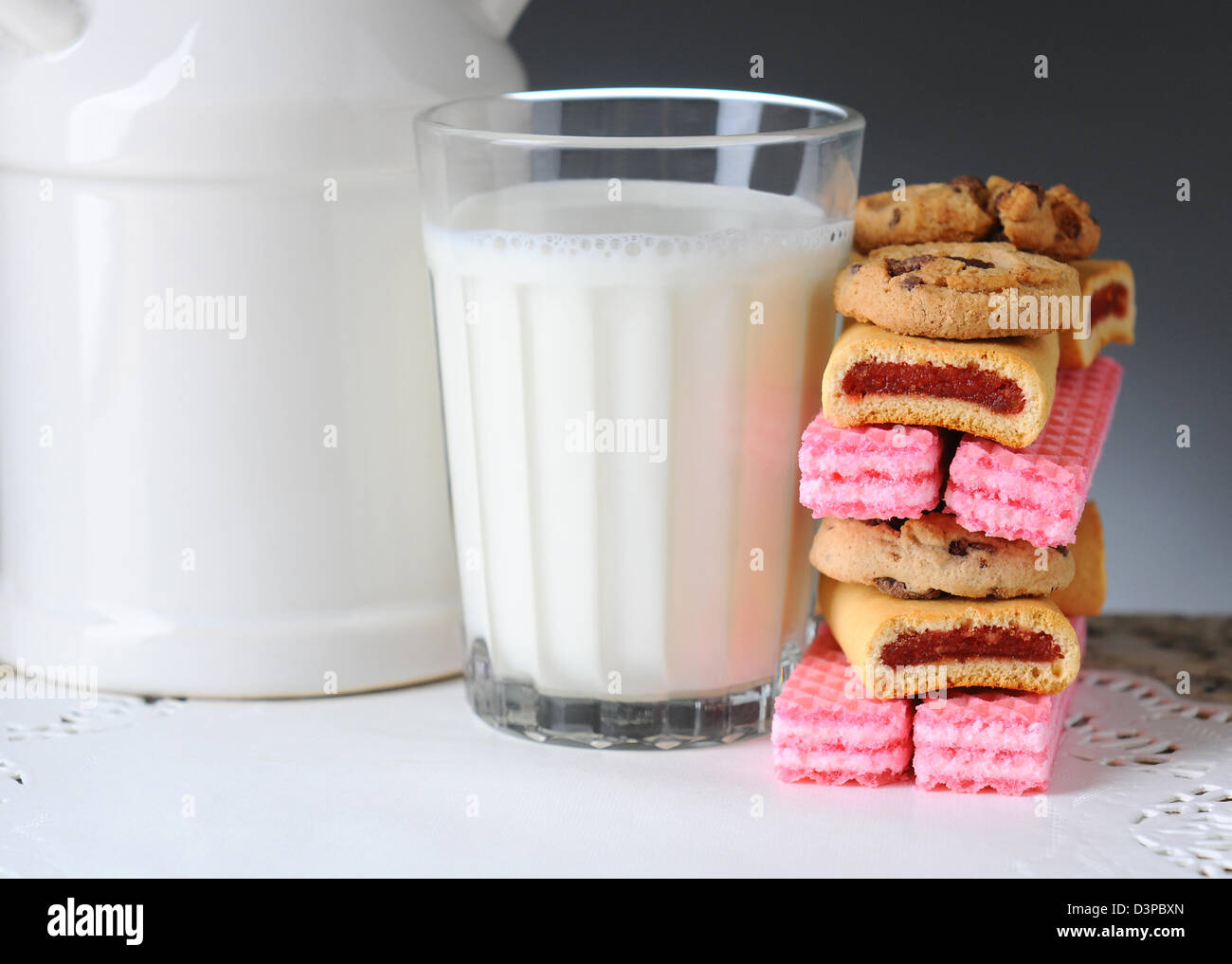 Nahaufnahme von einem Glas Milch mit einem Stack von sortierten Cookies. Querformat auf eine leichte bis dunkelgrauen Hintergrund. Stockfoto