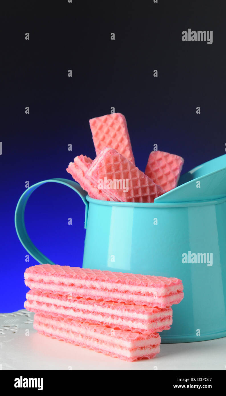 Nahaufnahme von einem blauen Zinn Krug gefüllt mit rosa Zucker Wafer Cookies, vertikalen Format mit einem Licht auf dunkelblauem Hintergrund. Stockfoto