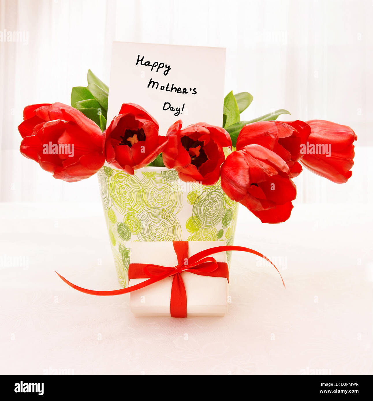 Frische rote Tulpe Blumen in schönen Vase mit Papier-Gruß-Postkarte auf der Tabelle, kleine weiße Geschenkbox Stockfoto