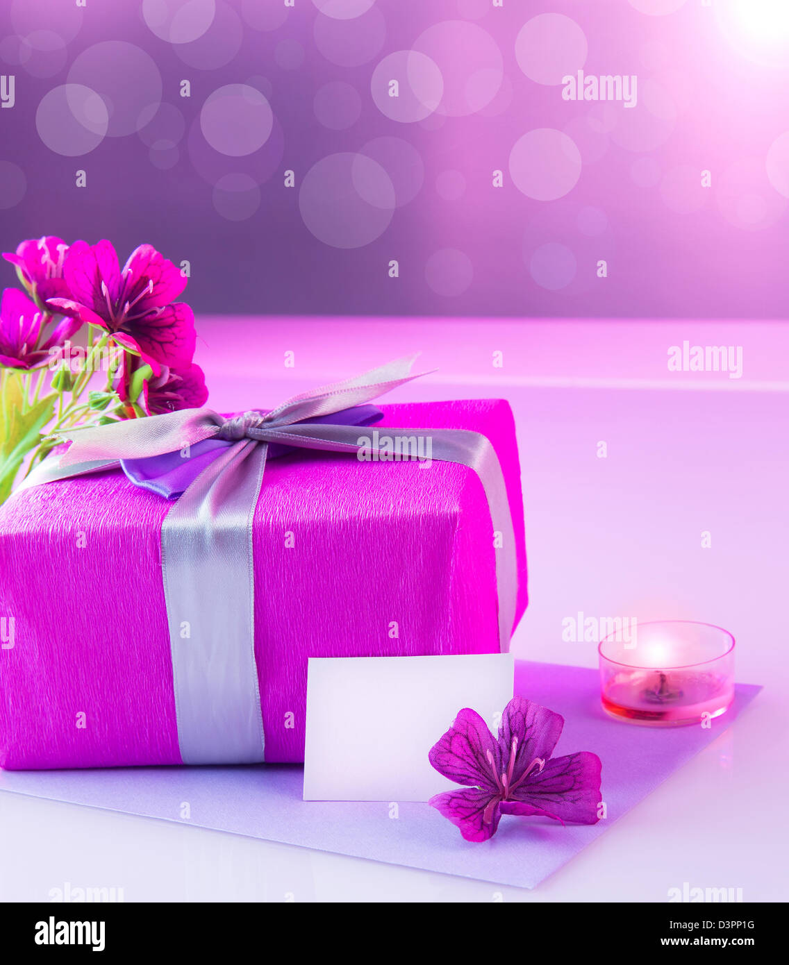 Bild des großen rosa Kasten mit weißen leeren Grußkarte auf dem Tisch zu präsentieren und dekoriert mit frischen Blumen Blumenstrauß und Kerze Stockfoto
