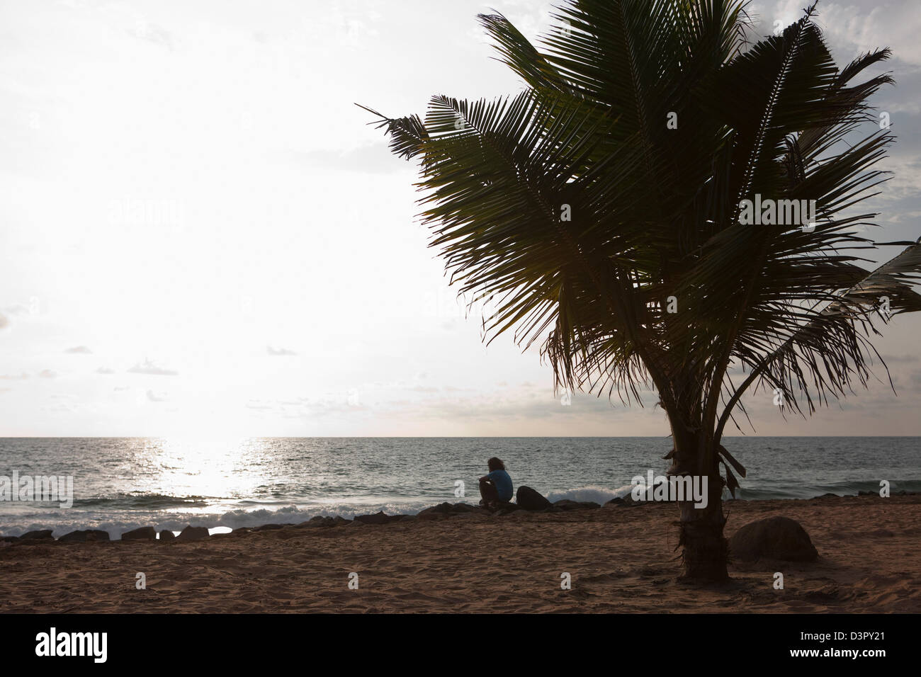 Person sitzt am Strand bei Sonnenuntergang, Arabisches Meer, Kerala, Indien Stockfoto