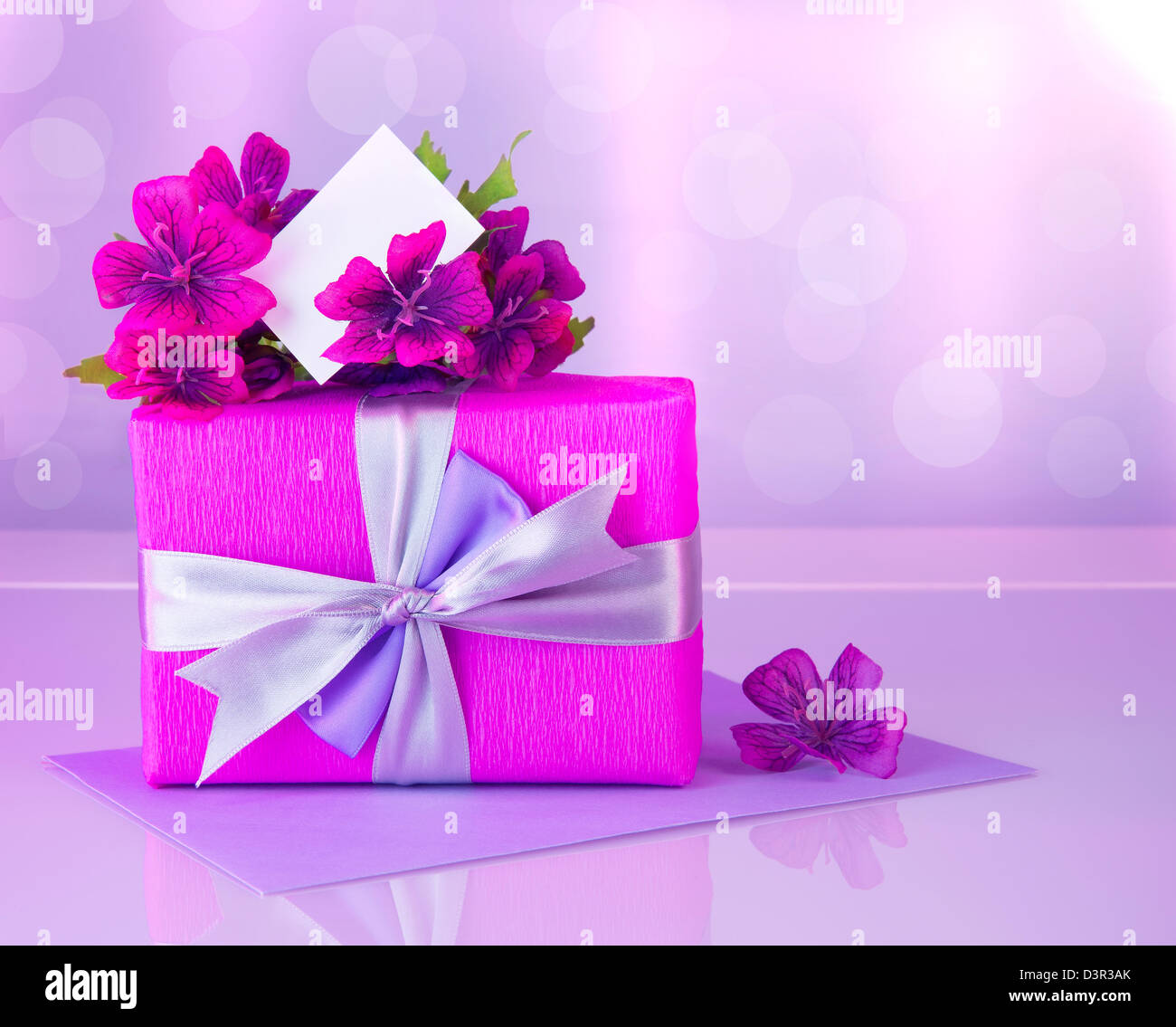 Bild von rosa Geschenkbox mit lila Seidenband, wunderschöne violette wilde Blumen Bukett, weiße leere Grußkarte Stockfoto