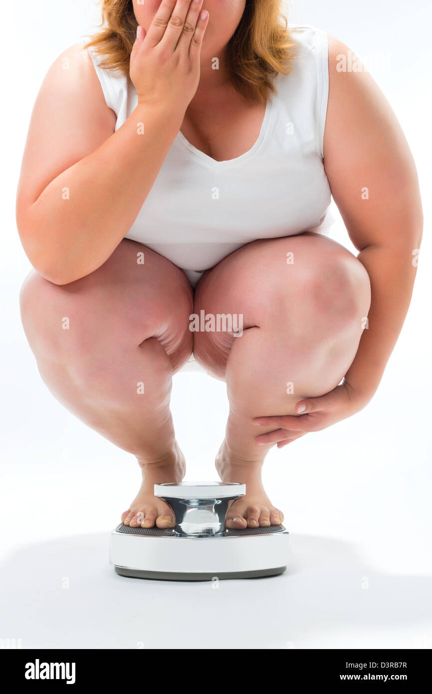 Ernährung und Gewichtsabnahme, übergewichtige junge Frau kauert auf einer Skala messen ihr Gewicht Stockfoto