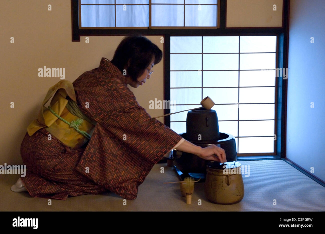 Frau in Tatami Matten Teestube bereitet Teezeremonie Utensilien: Kama Wasserkocher, Chasen Schneebesen, Mizusashi Wasserkrug und Hishaku Schöpfkelle. Stockfoto