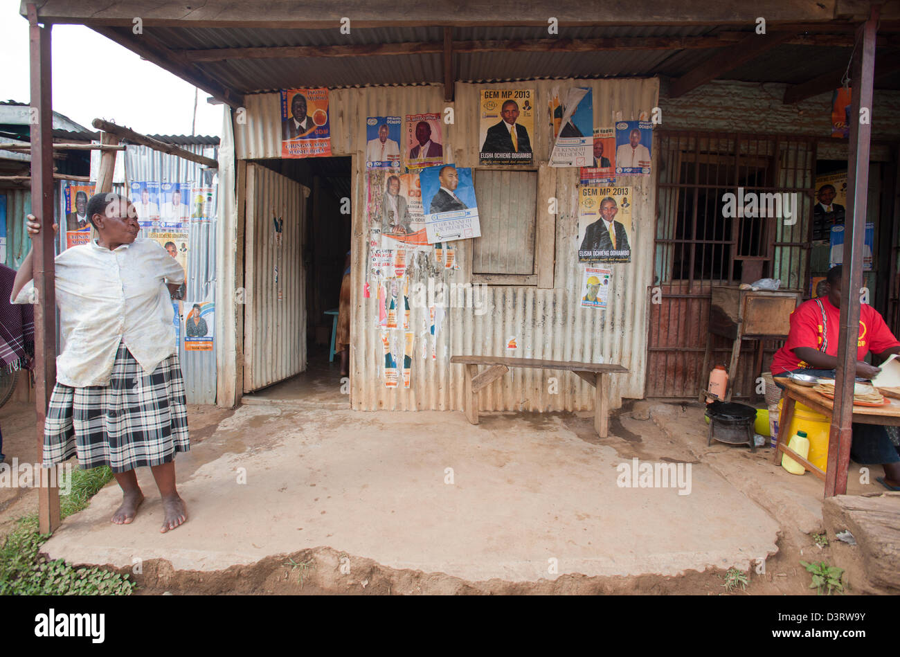 Dame stehend infront von Shop bedeckt mit politischen Plakaten, Yala, Provinz Nyanza, Kenia, Februar 2013. Stockfoto