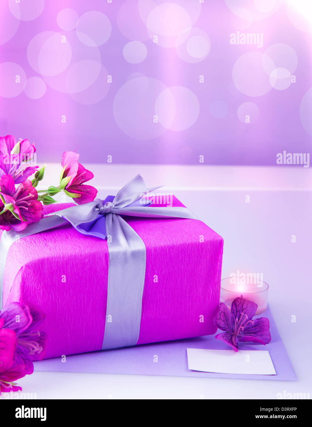 Foto von rosa Geschenkbox mit lila Seidenband, wunderschöne violette wilde Blumen Blumenstrauß, Kerze und weiße leere Grußkarte Stockfoto