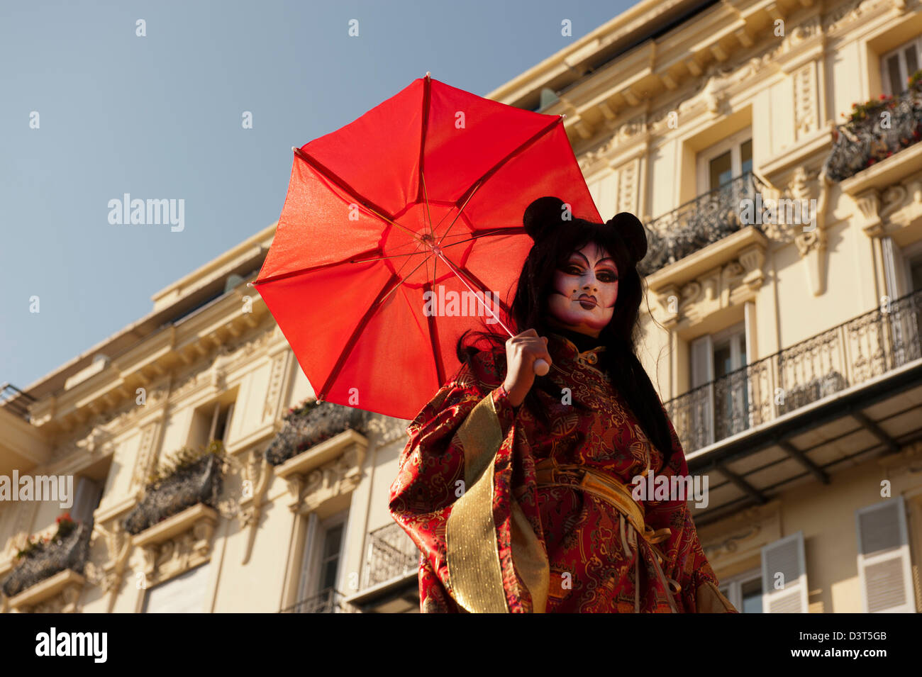 Geisha mit leuchtend roten Regenschirm sitzt oben auf einen Schwimmer in der Karneval von Nizza-parade Stockfoto