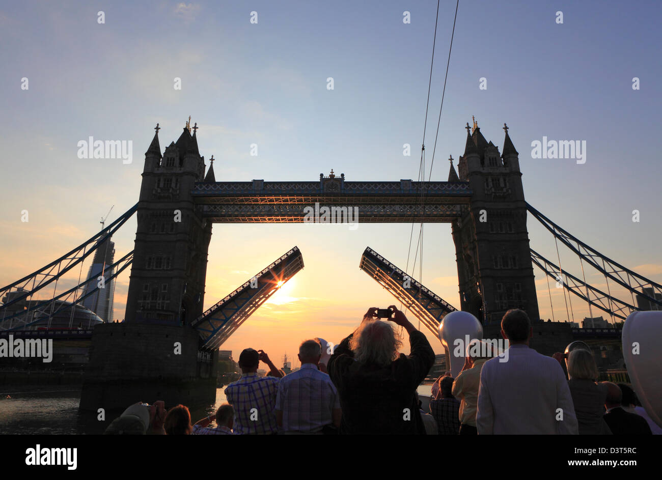 Touristen fotografieren die Tower Bridge, die für ihr Boot aufgezogen wurde, um durch die Brücke zu fahren, bei Sonnenuntergang von einem Boot auf der Themse London England GB. Stockfoto