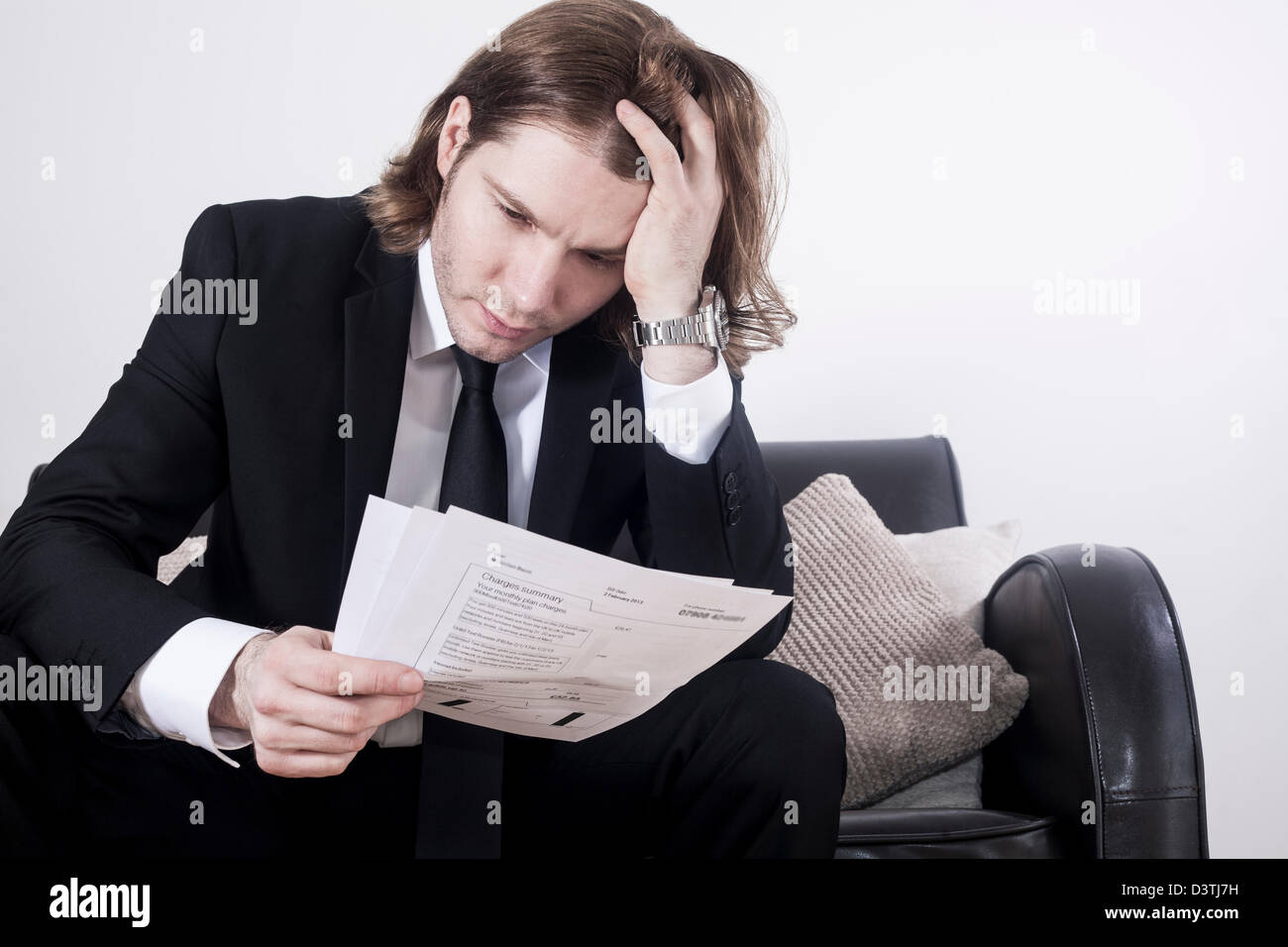 weißer Mann in intelligente Business-Anzug mit einer Hand in seiner langen braunen Haaren und die andere Hand halten / Inspektion Rechnungen Stockfoto