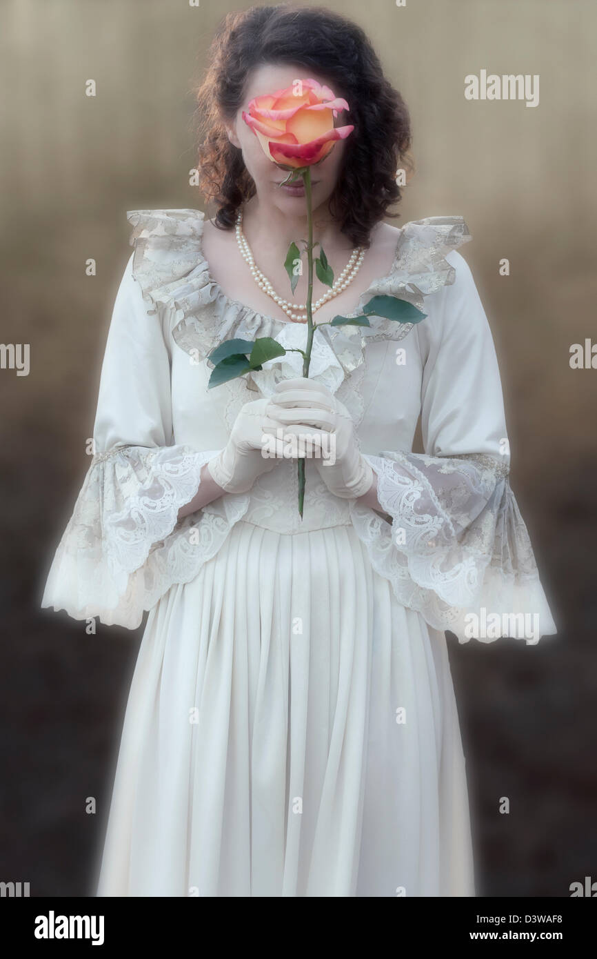 eine Dame in einem viktorianischen Kleid ist eine Rose vor ihr Gesicht halten. Stockfoto