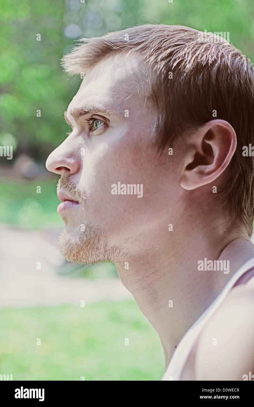 Porträt von einem schönen jungen Mann gegen grünen Wald. Profil Stockfoto