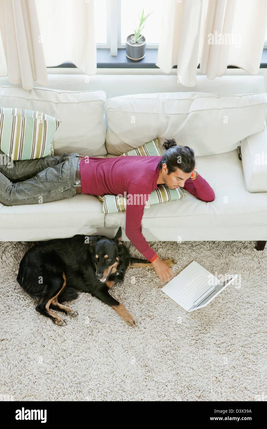 Eine lässige Hispanic-Latino Jüngling unterhaltsam sein Haustier Hund surfen Internet mit Laptop Stockfoto