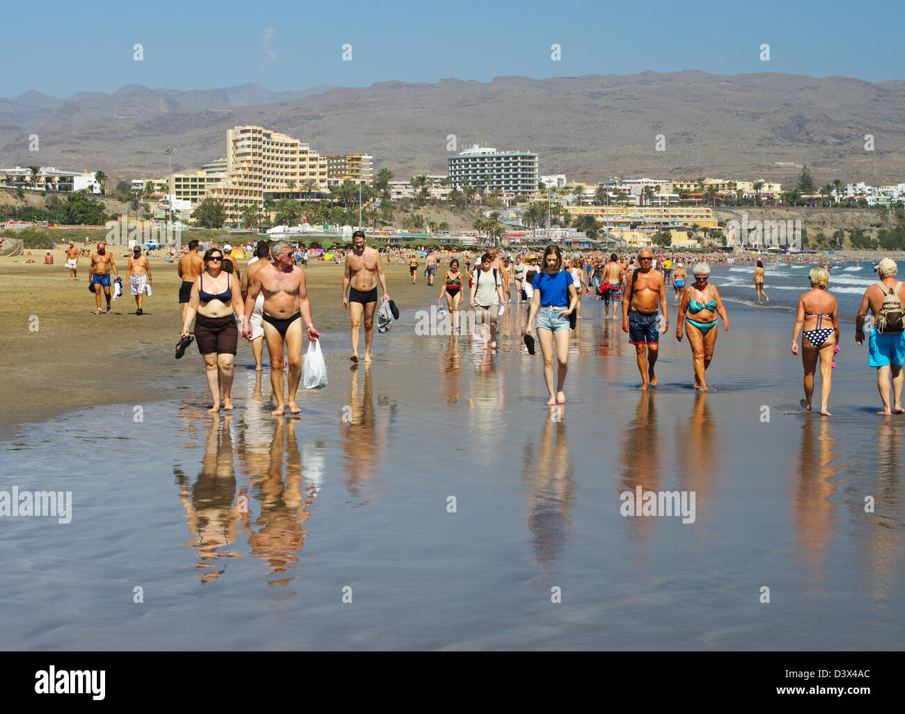 Gruppe von Menschen zu Fuß auf dem nassen Sand am Playa del Inglés, Gran Canaria Stockfoto